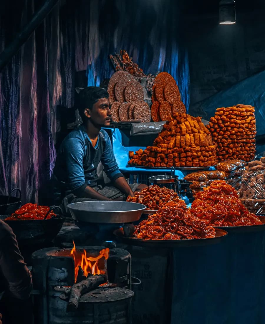 A halwai at his bhatti beside stacks of fresh jalebi