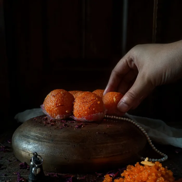 A hand placing a laddoo on a brass stand