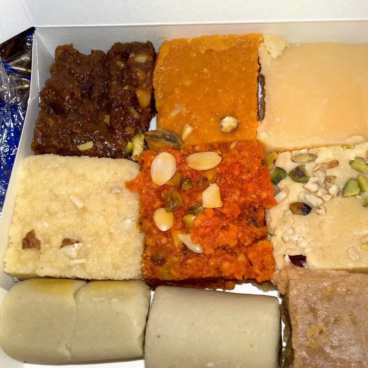 A box packed with assorted barfi topped with almonds and pistachios