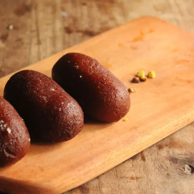Three dark kala jamun on a wooden board