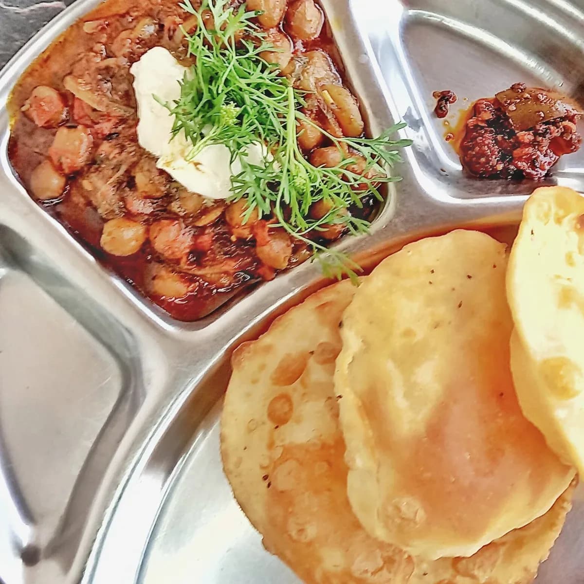 Puffed puris with spiced chole on a steel thali